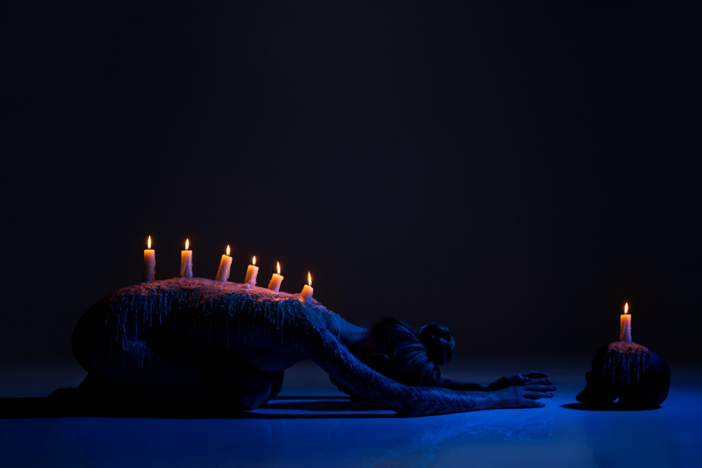 Burning candles on back of lady bowing down in darkness de Andrey Guryanov