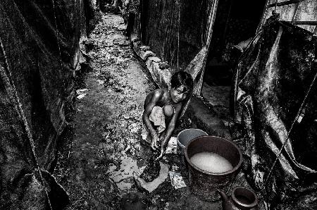 Rohingya refugee girl cleaning clothes in the street, in front of her house - Bangladesh